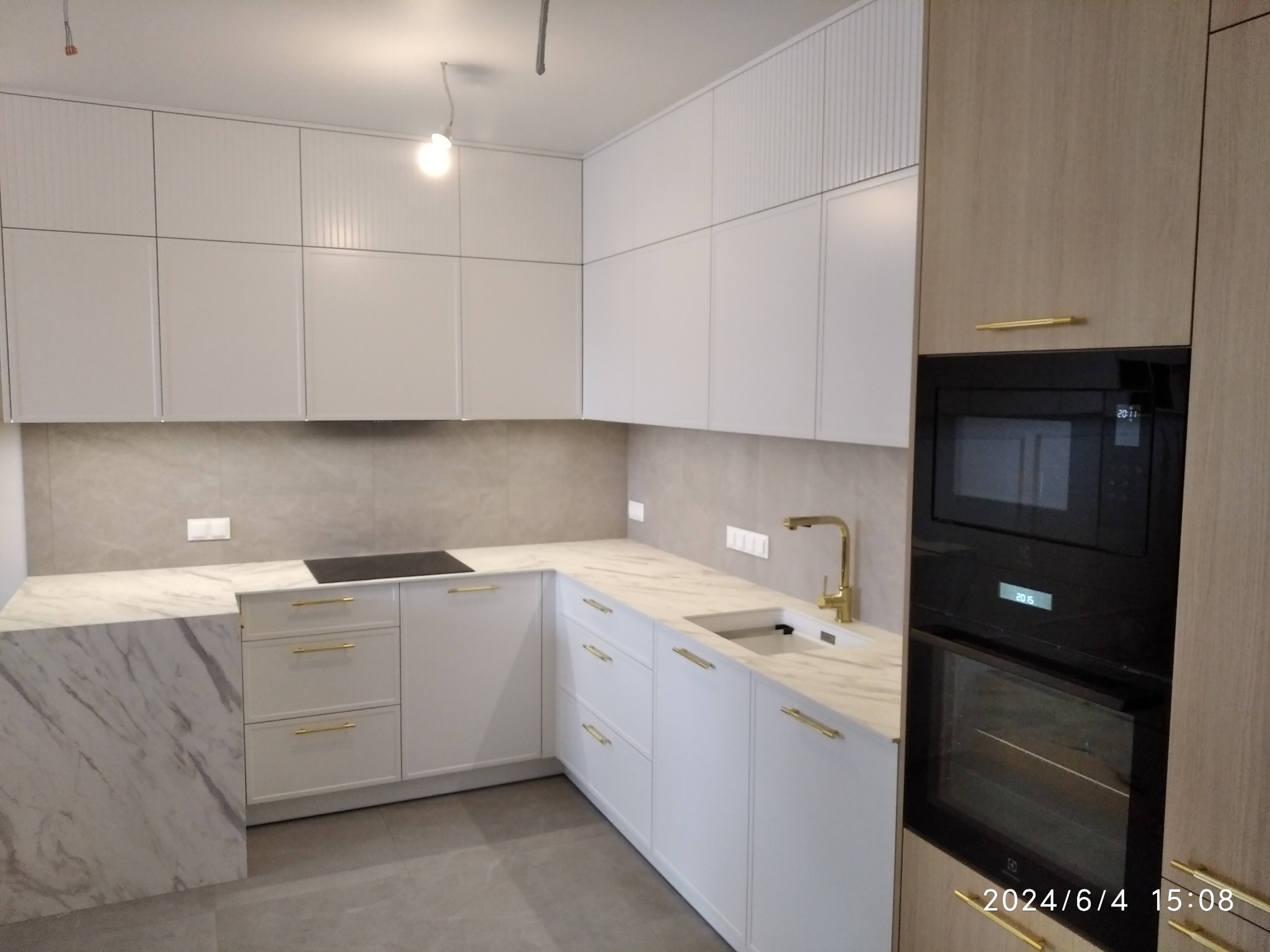 Nowoczesna kuchnia w jasnych barwach z marmurowym blatem, złotymi uchwytami i wbudowanym sprzętem AGD, sfotografowana z niskiego kąta.