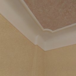 Jan & Co - Wykończony narożnik pokoju z beżową ścianą o fakturze spękań i sufitem z dekoracyjnym wzorem, oddzielonym białym, profilowanym gzymsem.