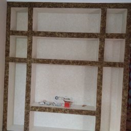 Jan & Co - Ściana z wnękami, wykończona tapetą w odcieniach beżu i brązu, z widocznymi materiałami budowlanymi na jednej z półek.