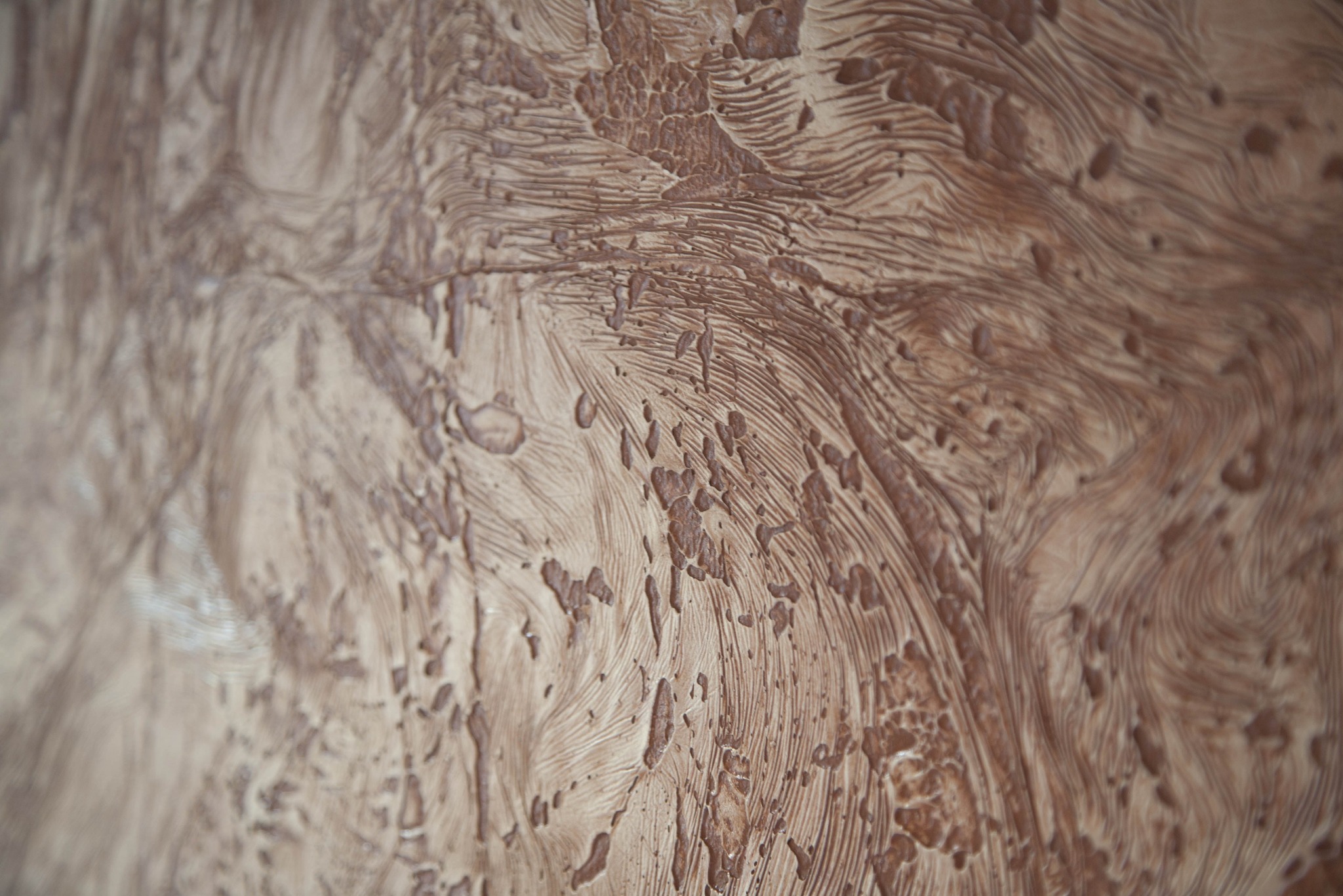 Tekstura ściany z efektem dekoracyjnym, beżowo-brązowa, z wyraźnie widocznymi smugami i wypukłościami imitującymi naturalne wzory drewna.