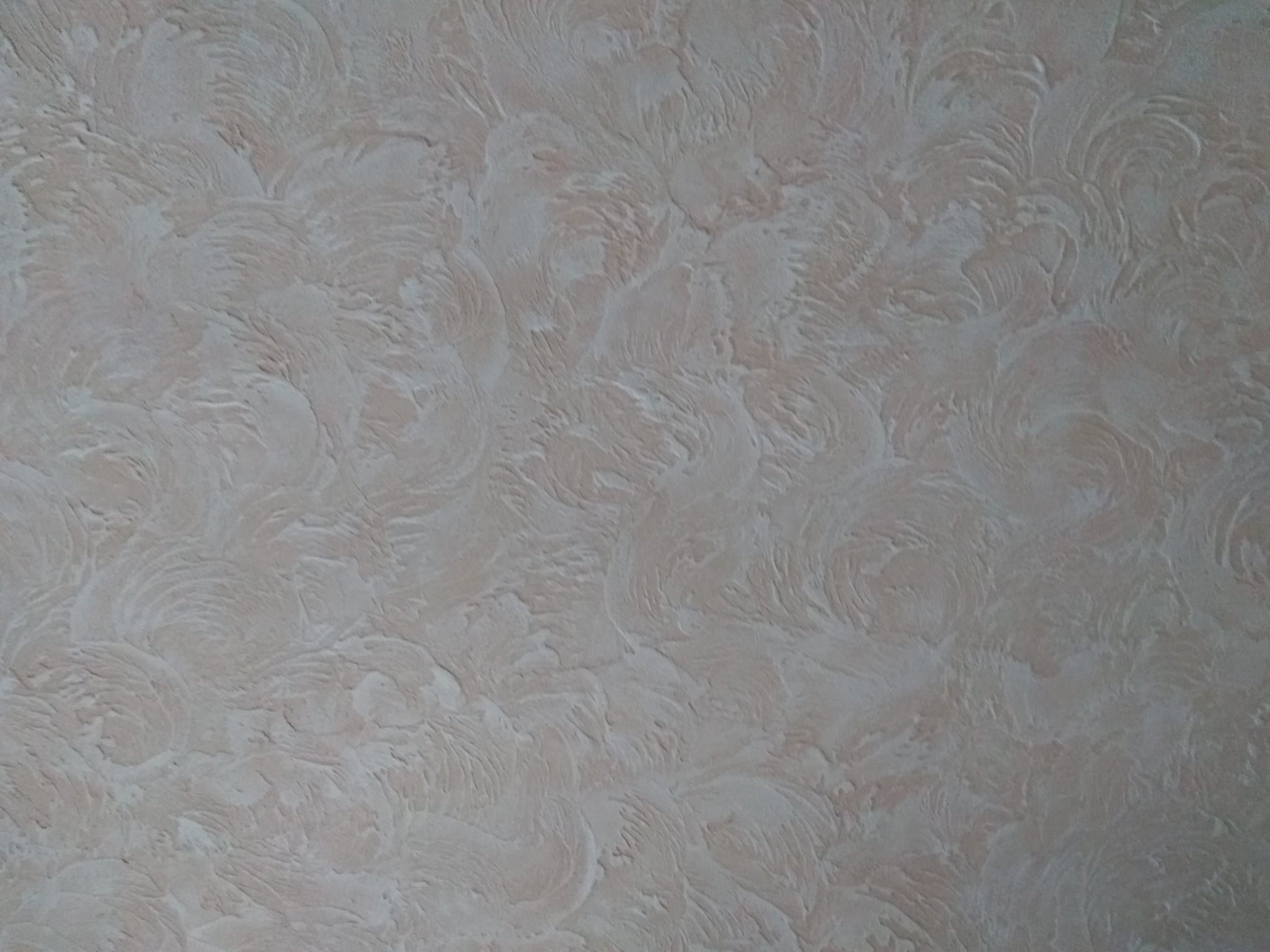 Beżowa ściana z dekoracyjną fakturą imitującą wzór piór lub liści, wykonana techniką malarską lub tynkarską.