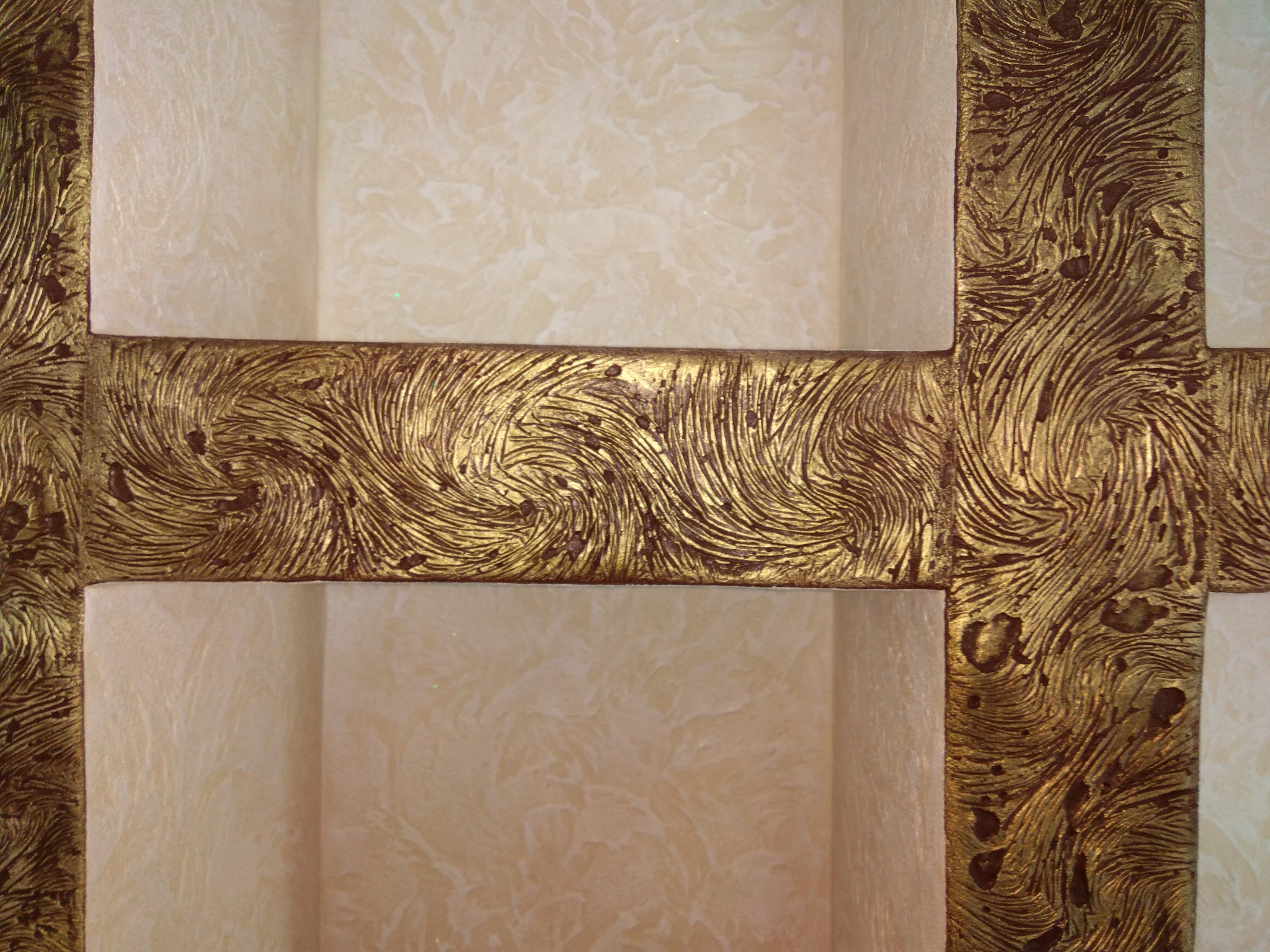 Dekoracyjna ściana z efektem stiuku w odcieniach beżu, podkreślona złotymi, teksturowanymi listwami tworzącymi geometryczny wzór.