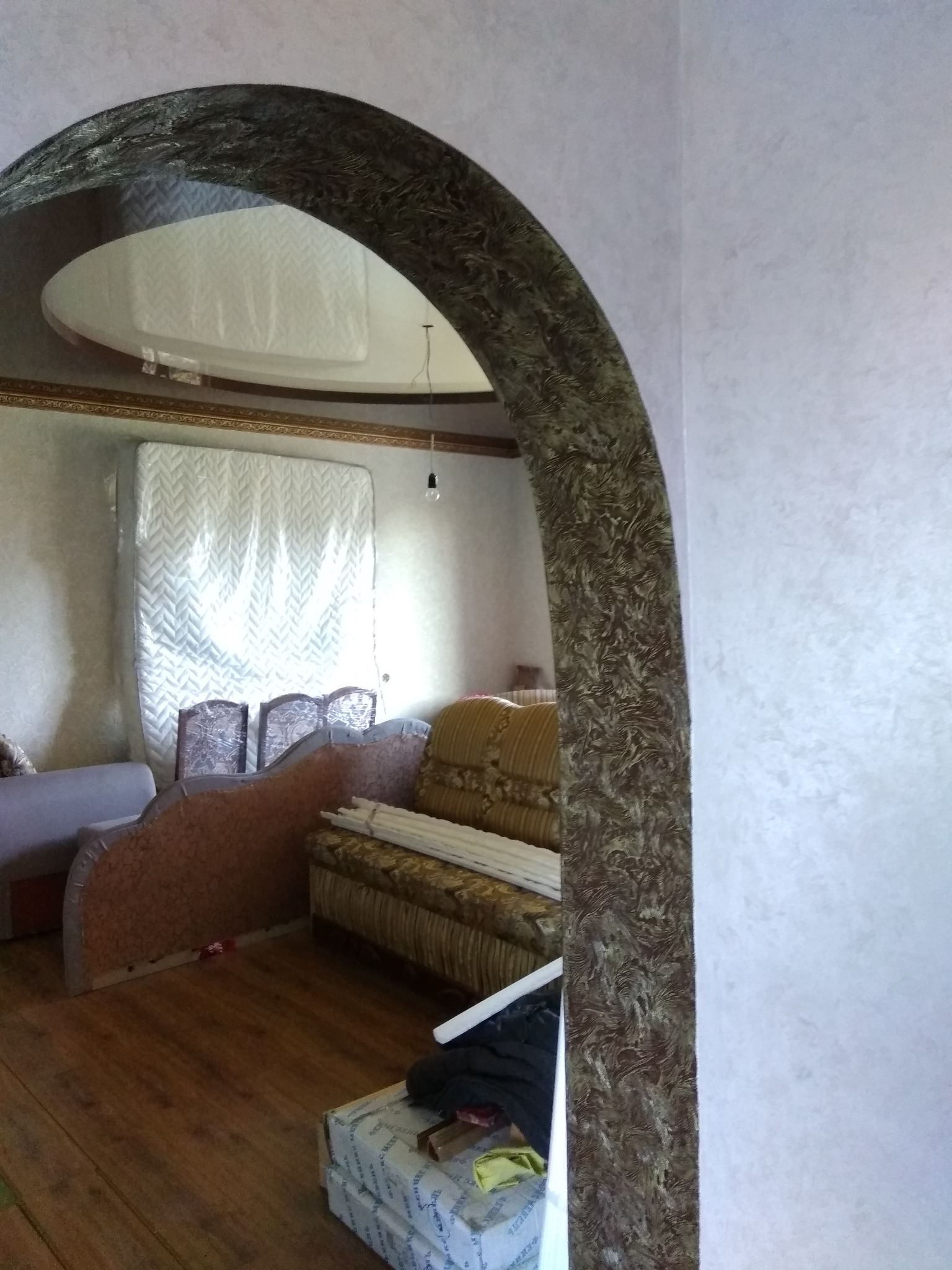 Wykończony łuk wejściowy z dekoracyjnym wzorem w mieszkaniu w Warszawie, widoczne meble w trakcie remontu i zabezpieczony materac.