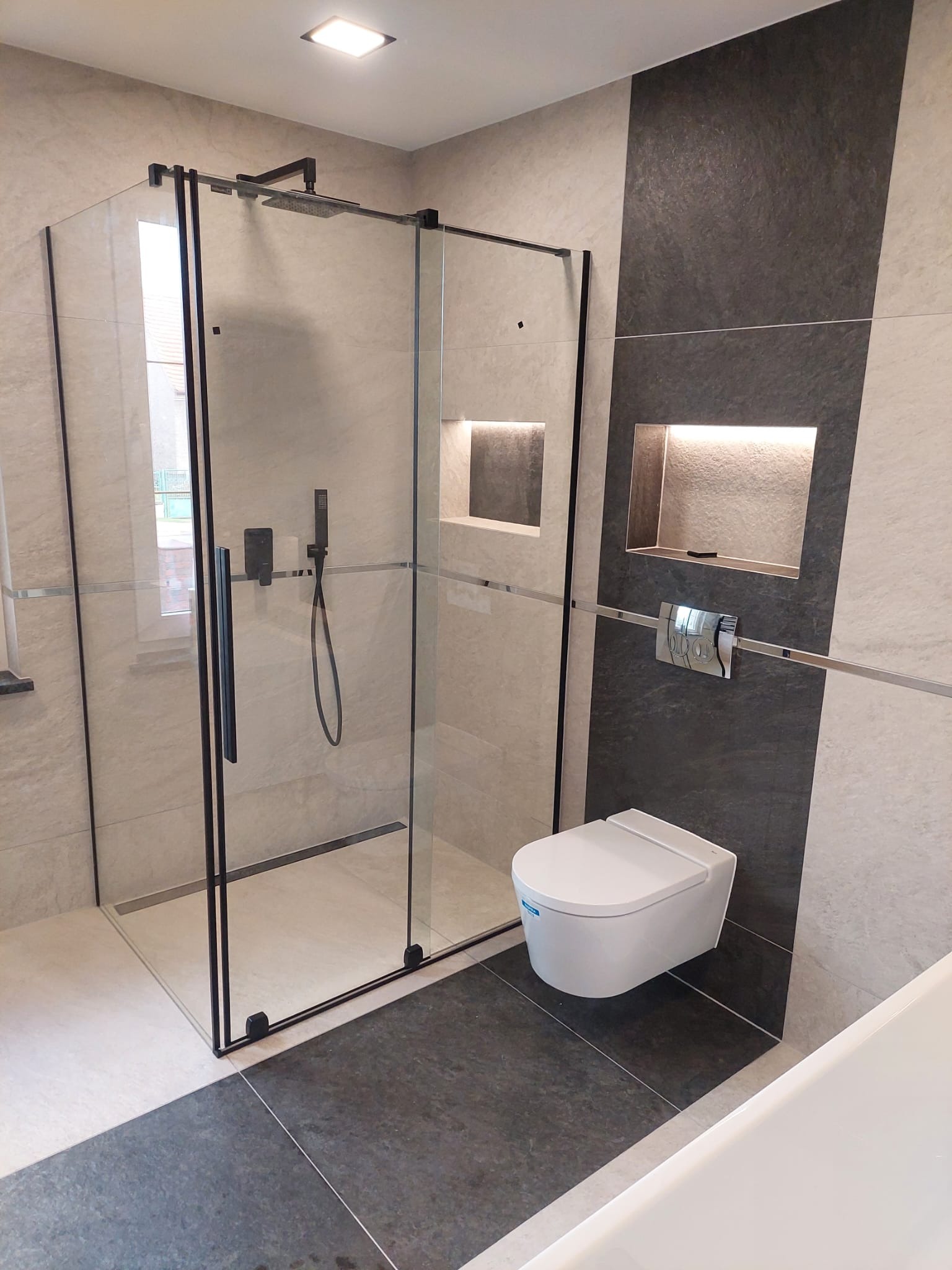 Nowoczesna łazienka w Wojska z kabiną prysznicową typu walk-in z czarnymi profilami, podwieszaną toaletą i wnękami ściennymi z podświetleniem LED.