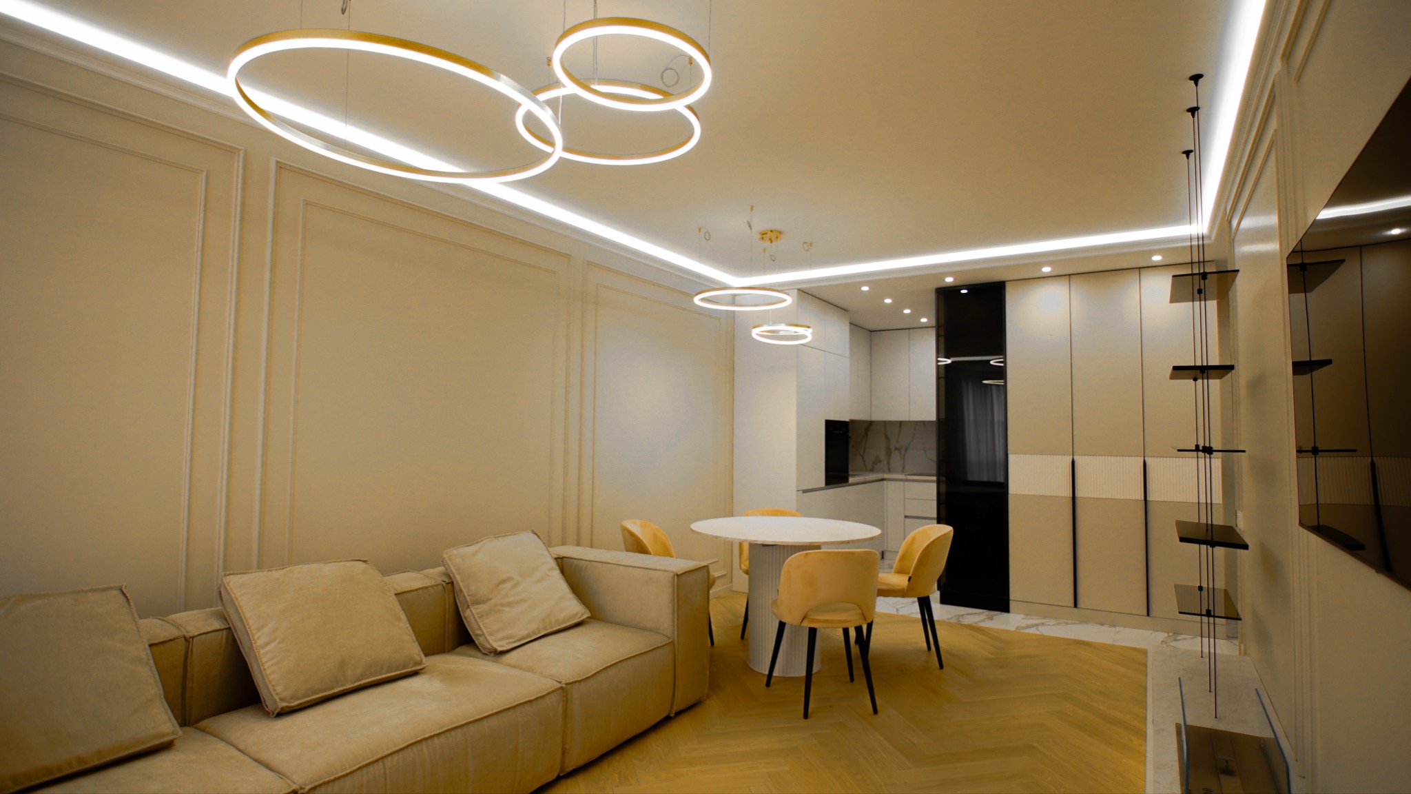 Salon z aneksem kuchennym w odcieniach beżu i bieli, z okrągłym stołem, żółtymi krzesłami, beżową sofą i wiszącymi lampami w kształcie okręgów.