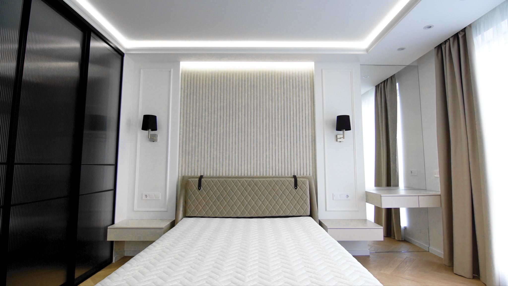 Nowoczesna sypialnia z łóżkiem z pikowanym zagłówkiem, czarnymi kinkietami i przesuwną szafą z ryflowanego szkła.