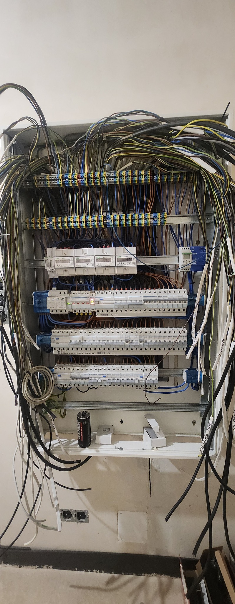 Rozdzielnica elektryczna w trakcie montażu w Bydgoszczy, widoczne liczne przewody, bezpieczniki i osprzęt. Na dole puszka z napojem energetycznym i opakowania po elementach instalacji.