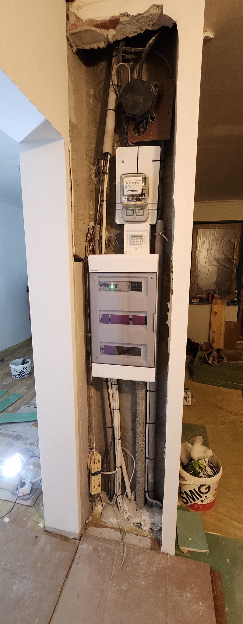 Rozdzielnica elektryczna z licznikiem i przewodami w trakcie montażu w surowym stanie wykończenia wnętrza.