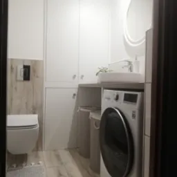 Nowoczesna łazienka z pralką LG pod umywalką, białe szafki w zabudowie, okrągłe lustro i drewnopodobne płytki na podłodze i ścianie, widok zza framugi drzwi.