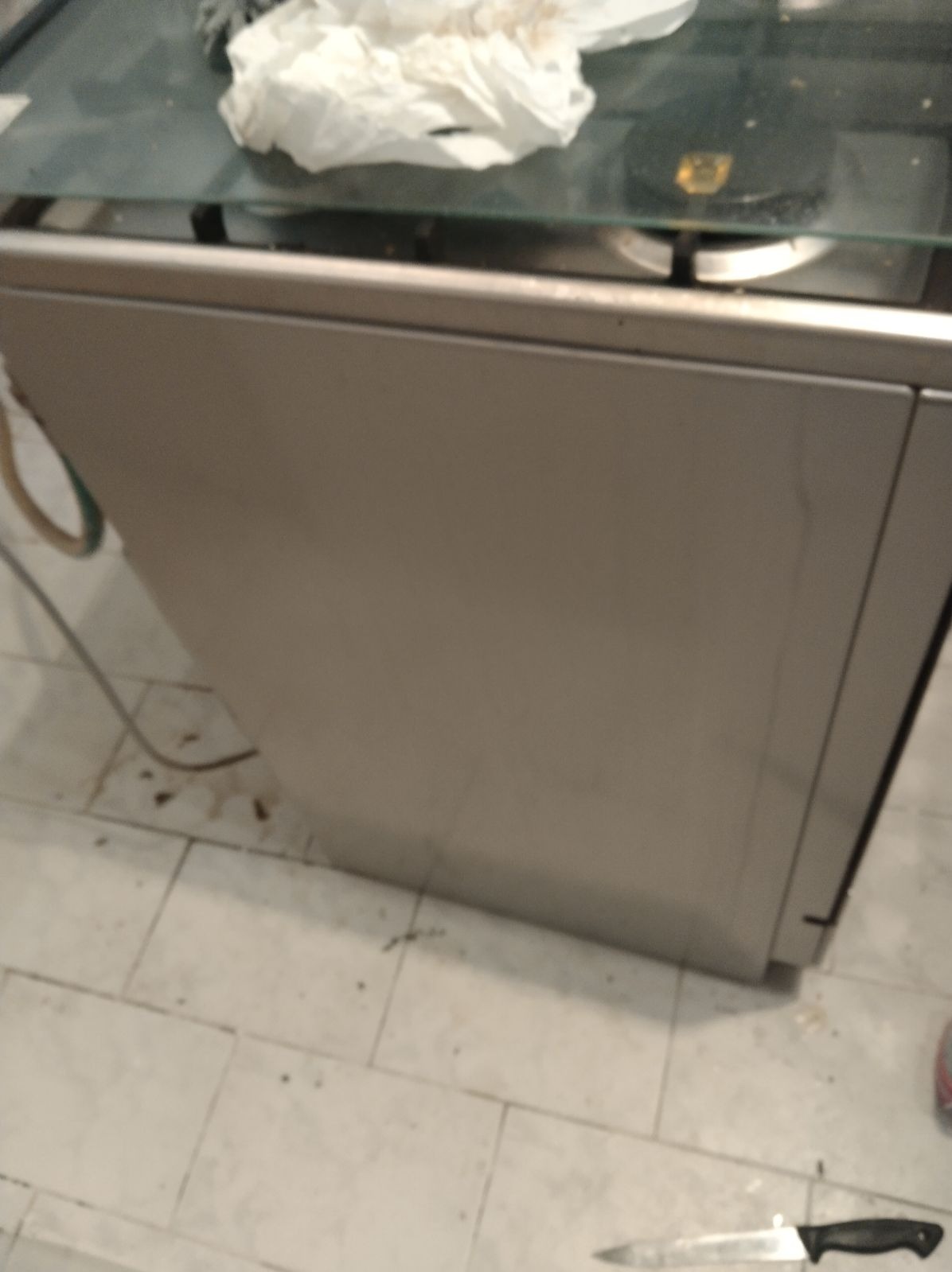 Brudna kuchnia z resztkami jedzenia na płycie i pod szafką, nóż leżący na podłodze.