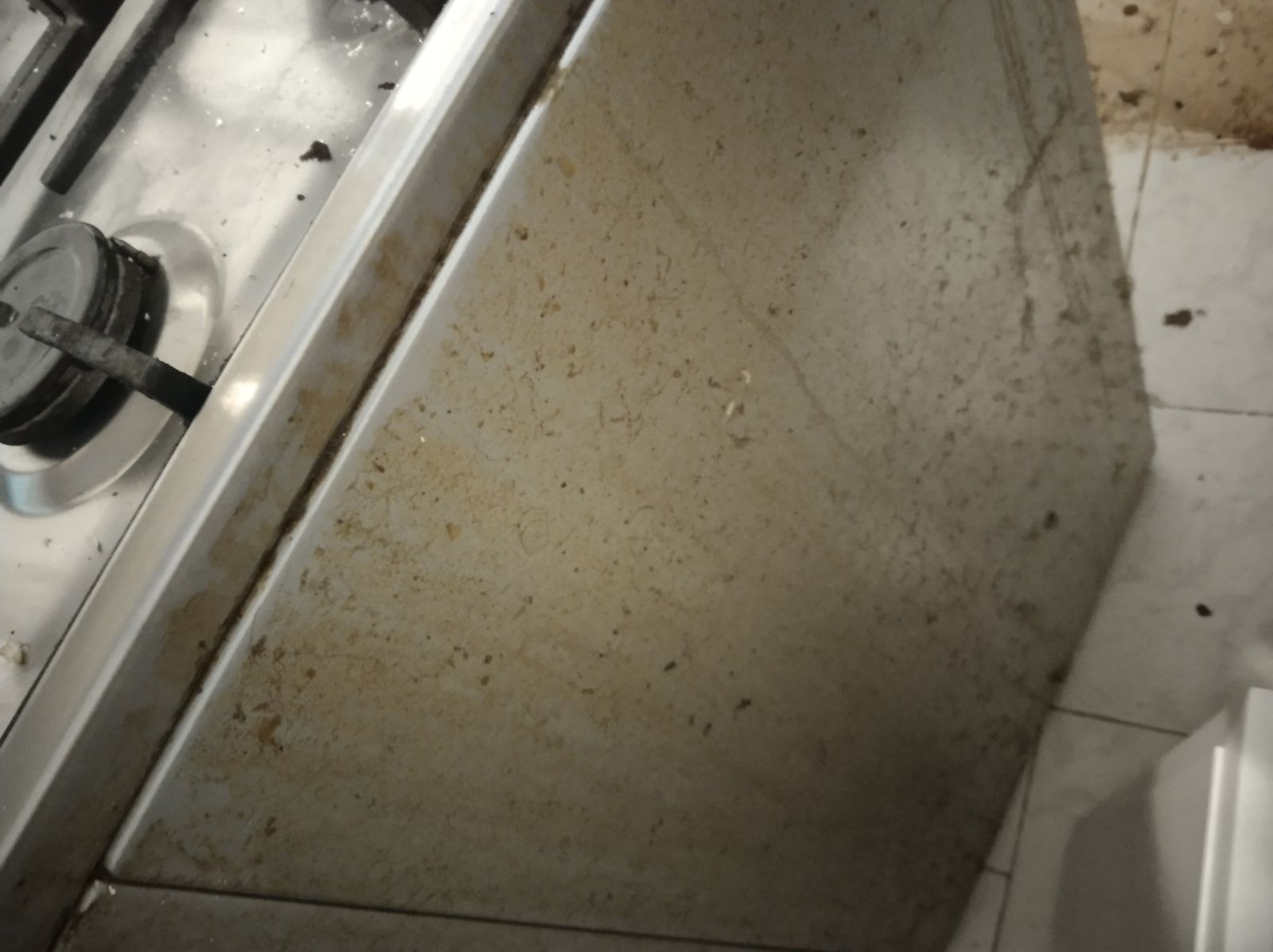 Zabrudzona płyta gazowa i bok szafki kuchennej pokryte zaschniętym brudem i plamami, widoczne z bliska pod kątem.