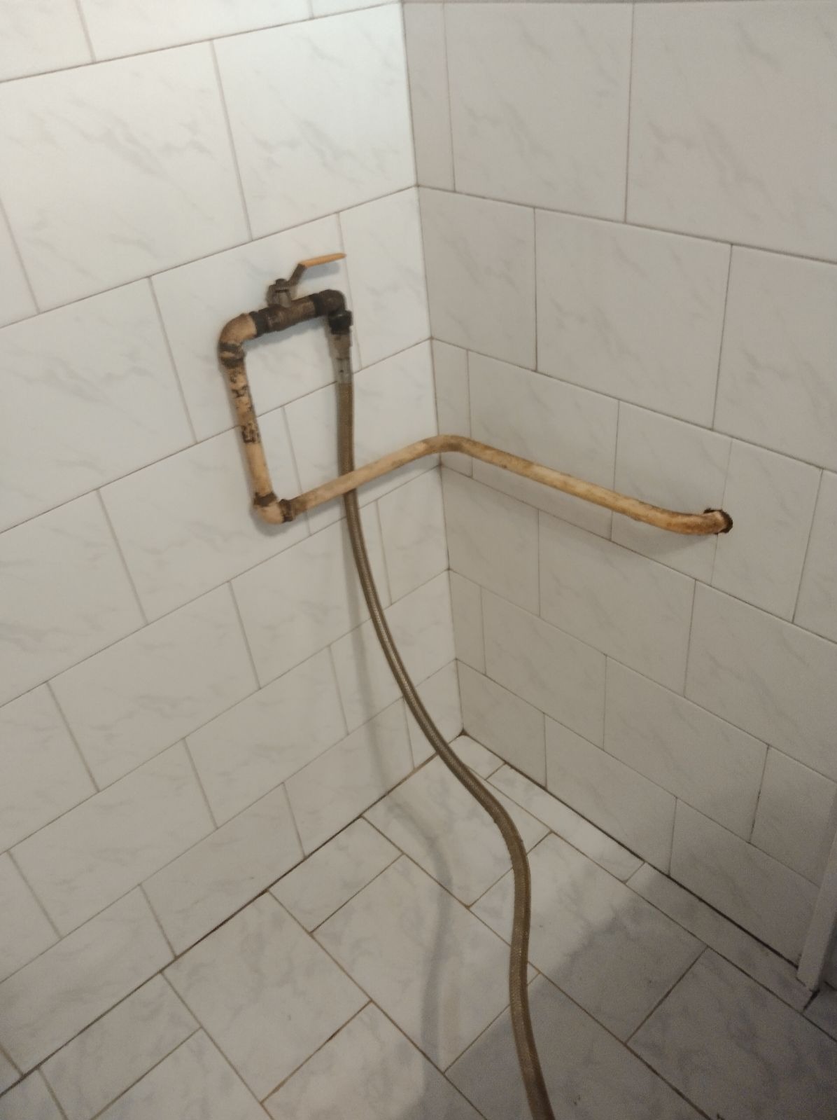 Ujęcie fragmentu łazienki z odłączonymi, starymi rurami i zaworem, widoczne ślady rdzy i zabrudzeń na białych płytkach.