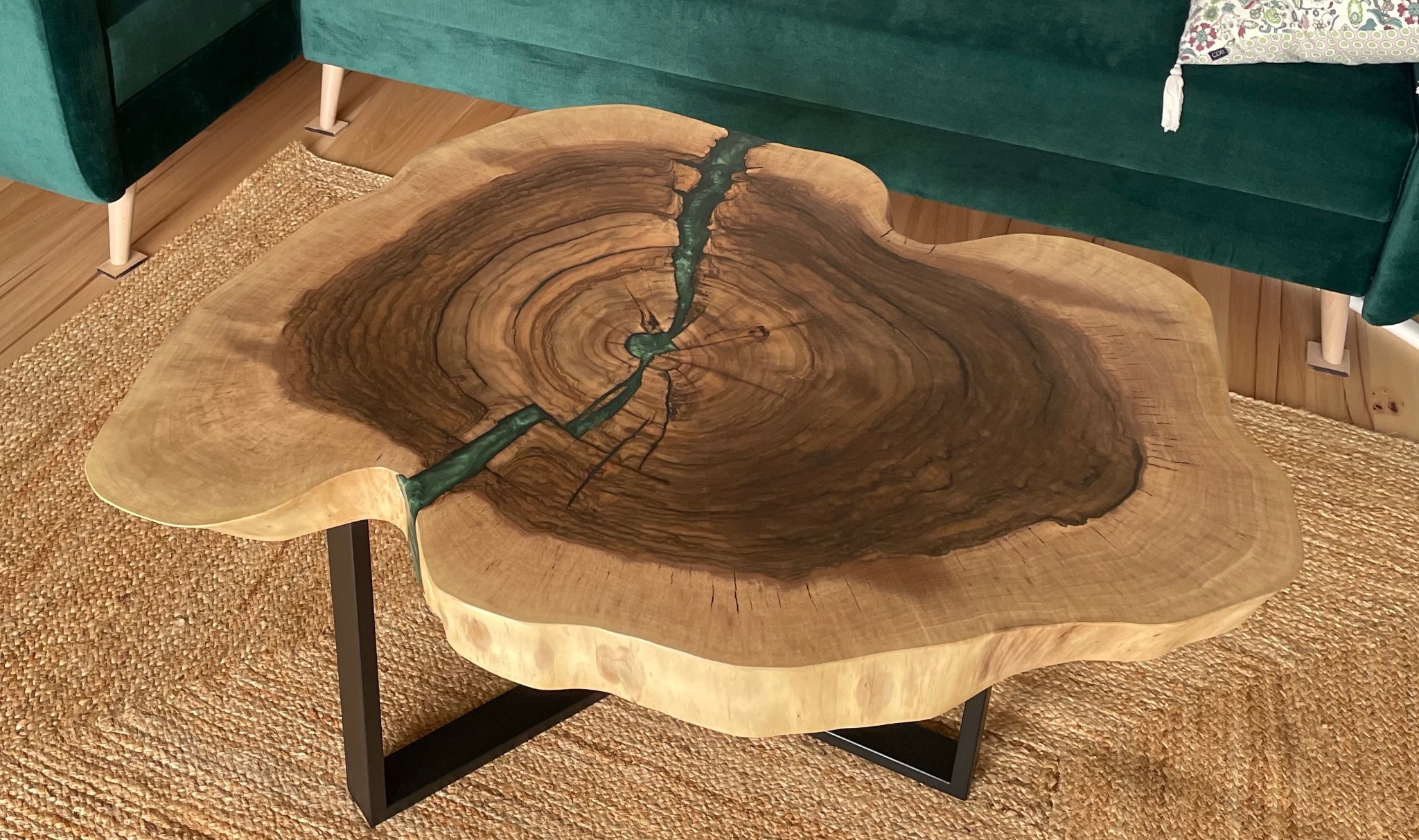 Stolik kawowy z blatem z plastra drewna z żywicą epoksydową w kolorze zielonym, na metalowych nogach w salonie z zieloną sofą.