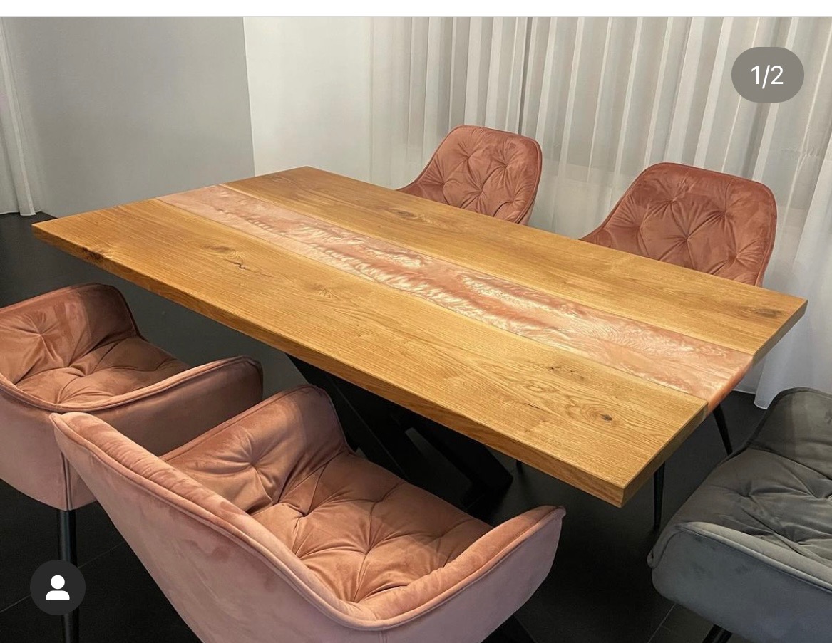 Stół z blatem z jasnego drewna z żywicą epoksydową w odcieniach różu, ustawiony na czarnych, metalowych nogach, otoczony welurowymi krzesłami w kolorze pudrowego różu i szarości.