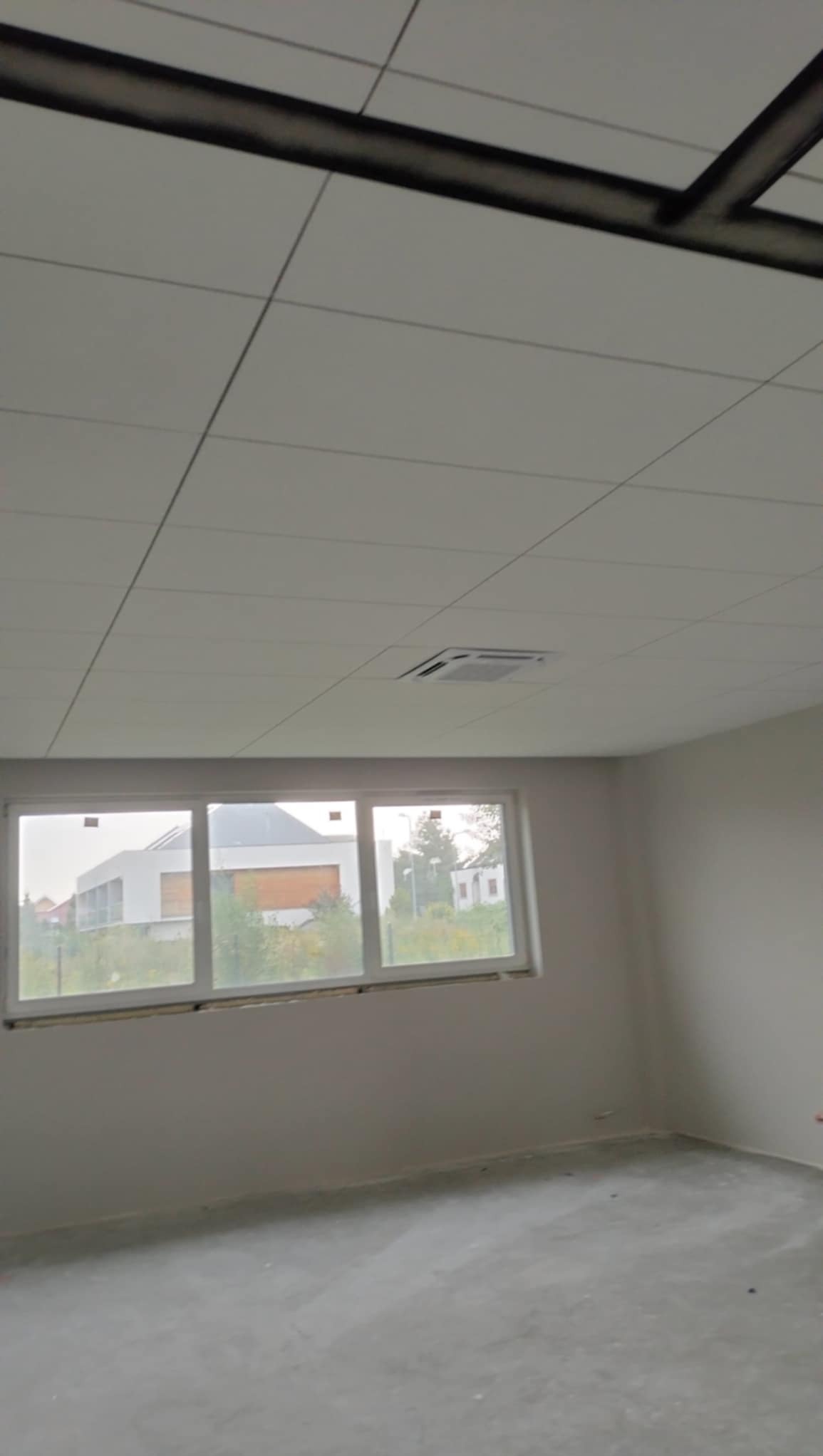 Płyty sufitowe kasetonowe z widoczną konstrukcją nośną i wbudowanym nawiewnikiem klimatyzacji w pomieszczeniu z oknem.