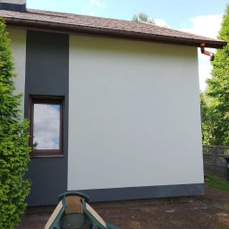 JU Solutions Janusz Utrata - Świeżo pomalowana ściana budynku z dwukolorową elewacją, widoczne okno z brązową ramą, rynna i sterta plastikowych krzeseł ogrodowych