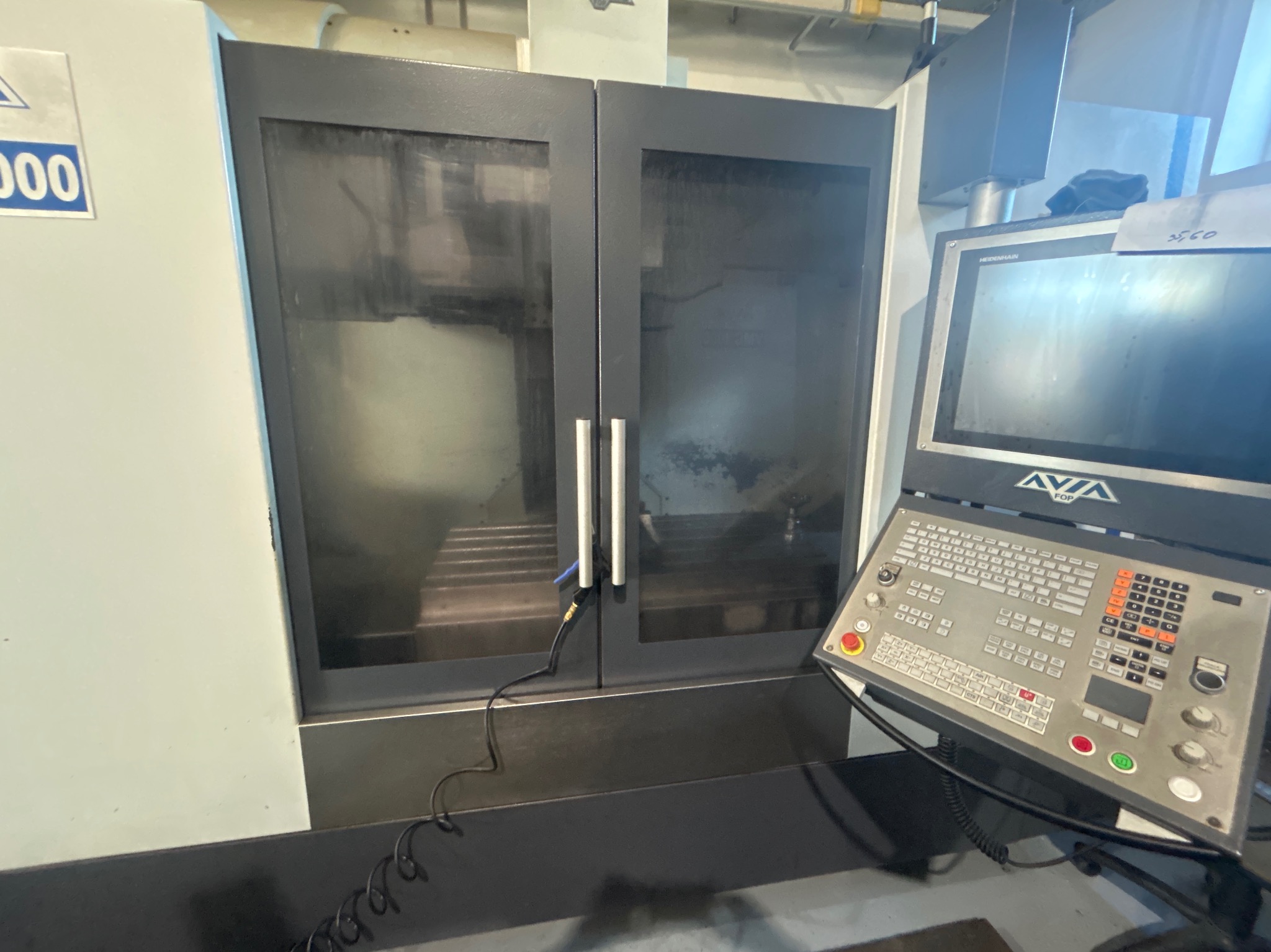 Zamknięta frezarka CNC z widocznym panelem sterowania Heidenhain i wnętrzem komory obróbczej z elementami mocującymi obrabiany materiał.