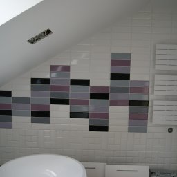 JARBUD - Białe płytki w łazience na poddaszu z dekoracyjnym pasem z czarnych, szarych i fioletowych płytek, grzejnik drabinkowy na ścianie, widoczne przewody elektryczne w suficie.