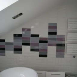 Białe płytki w łazience na poddaszu z dekoracyjnym pasem z czarnych, szarych i fioletowych płytek, grzejnik drabinkowy na ścianie, widoczne przewody elektryczne w suficie.