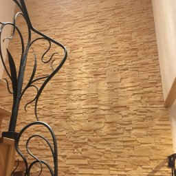 JARBUD - Ściana wykończona dekoracyjnym kamieniem w odcieniach beżu, widoczna z perspektywy schodów z ozdobną, kutą balustradą.