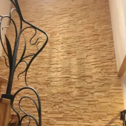 Ściana wykończona dekoracyjnym kamieniem w odcieniach beżu, widoczna z perspektywy schodów z ozdobną, kutą balustradą.