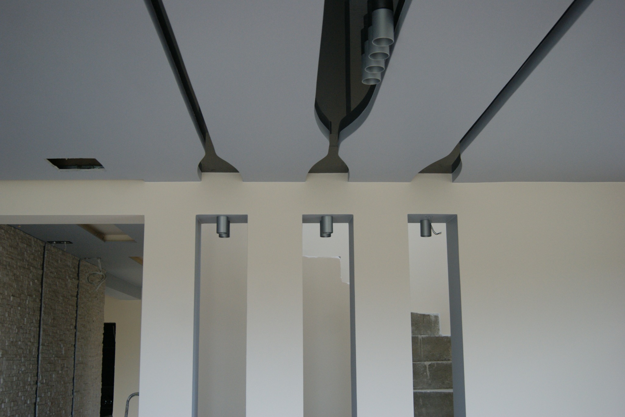 Nowoczesny sufit podwieszany z elementami dekoracyjnymi i oświetleniem, widoczne otwory w suficie i ścianie, wnętrze w trakcie prac wykończeniowych.