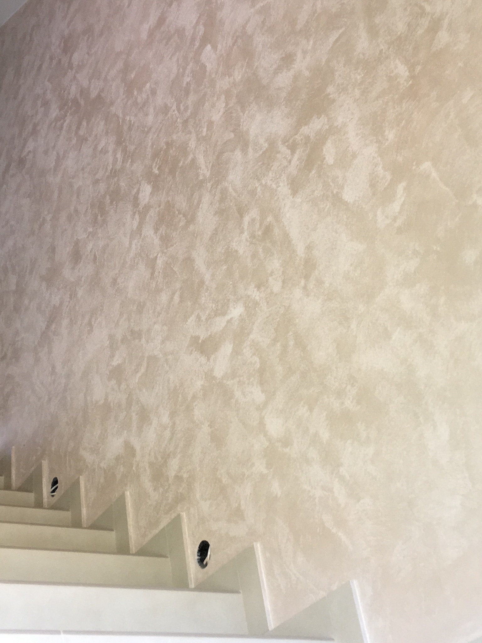 Ściana pokryta dekoracyjną gładzią w odcieniach beżu i bieli, widoczne schody z otworami na oświetlenie.