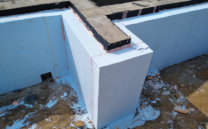 Izolacja termiczna fundamentów budynku z widocznymi płytami styropianowymi i zabezpieczeniem przeciwwilgociowym na styku z betonem.