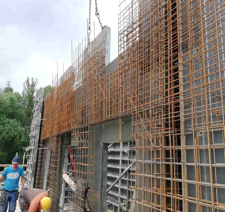 Montaż zbrojenia ściany fundamentowej z użyciem szalunków systemowych, widoczni dwaj pracownicy budowlani.