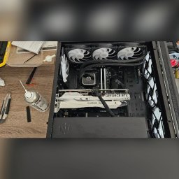 CompSecure Kacper Kamiński - Wnętrze komputera stacjonarnego z białą kartą graficzną GeForce RTX, chłodzeniem wodnym i trzema wentylatorami, obok leży puszka sprężonego powietrza i nożyk introligatorski.