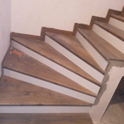 GLAZ TECH SZYSZKA RYSZARD - Wykończenie drewnopodobnych schodów z białymi podstopnicami w Chojnicach, widoczne pomarańczowe krzyżyki dystansowe przy płytkach.