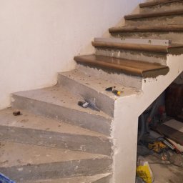 GLAZ TECH SZYSZKA RYSZARD - Betonowe schody w trakcie renowacji, z drewnianymi nakładkami na stopniach i poziomnicą, widoczne narzędzia i materiały budowlane w tle.