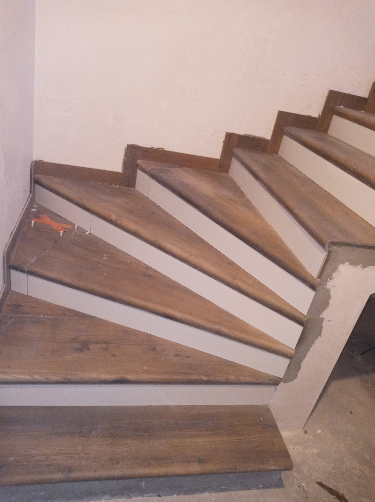 Wykończenie drewnopodobnych schodów z białymi podstopnicami w Chojnicach, widoczne pomarańczowe krzyżyki dystansowe przy płytkach.