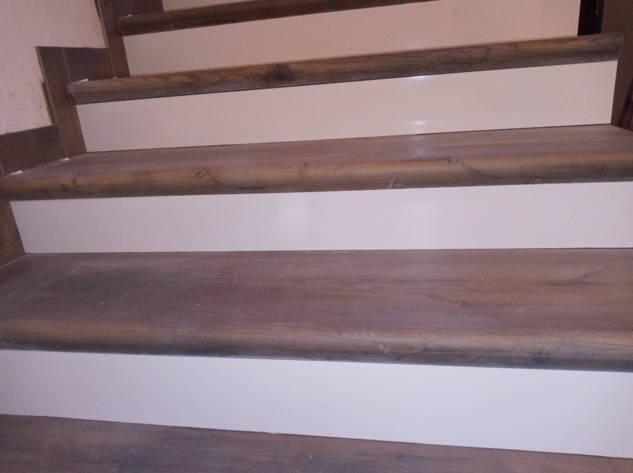 Bieg schodów z drewnianymi stopnicami o zaokrąglonych krawędziach i białymi podstopnicami, widok z dołu.