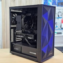 INsobi Konrad Sobiecki - Komputer stacjonarny do gier w czarnej obudowie z niebieskimi akcentami, widoczna karta graficzna GeForce RTX i chłodzenie procesora, umieszczony na drewnianym biurku na tle półek sklepowych.