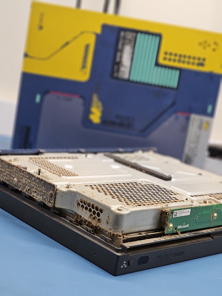 Otwarta obudowa zakurzonej konsoli Microsoft XBOX One S, widoczne elementy wewnętrzne przed czyszczeniem, w tle pudełko konsoli w edycji specjalnej.