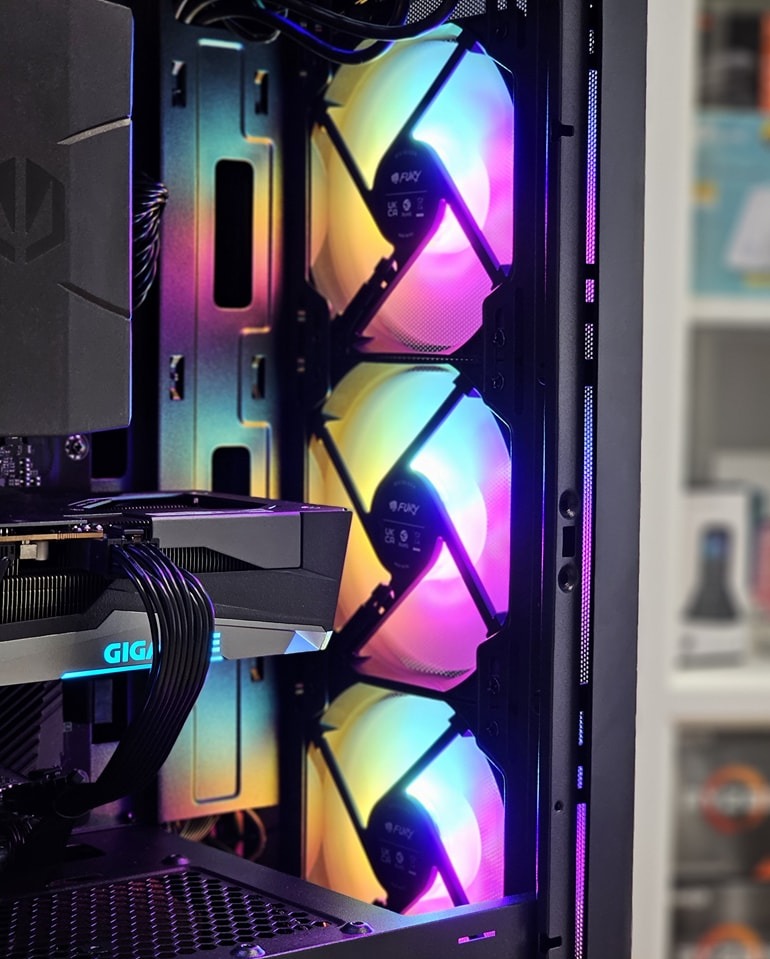 Wnętrze komputera stacjonarnego z trzema podświetlanymi wentylatorami RGB marki Fury, karta graficzna Gigabyte z niebieskim podświetleniem, widoczne kable w oplocie.
