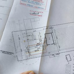 Emi-Maps Paweł Dołęga - Zatwierdzony projekt budowlany z naniesionymi instalacjami, pieczątką Starosty Pyrzyckiego i odręcznym podpisem. Widoczny fragment dłoni.