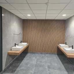 Miller. Bud. Oleh Miller - Nowoczesna łazienka publiczna z szarą marmurową podłogą i ścianami, drewnianą ścianą z pionowych listew oraz umywalkami nablatowymi na drewnianych blatach.
