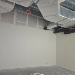 Miller. Bud. Oleh Miller - Wnętrze w trakcie prac wykończeniowych: ściany z płyt karton-gips z widocznymi łączeniami, instalacja wentylacyjna pod sufitem, przewody elektryczne na podłodze.