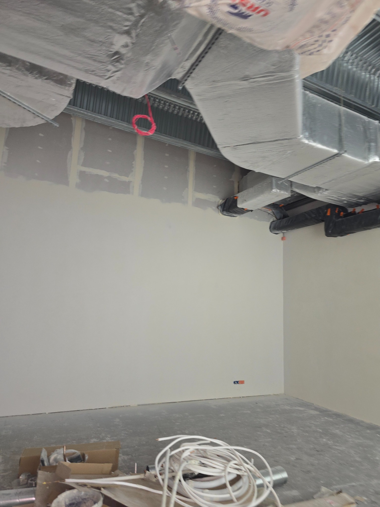 Wnętrze w trakcie prac wykończeniowych: ściany z płyt karton-gips z widocznymi łączeniami, instalacja wentylacyjna pod sufitem, przewody elektryczne na podłodze.