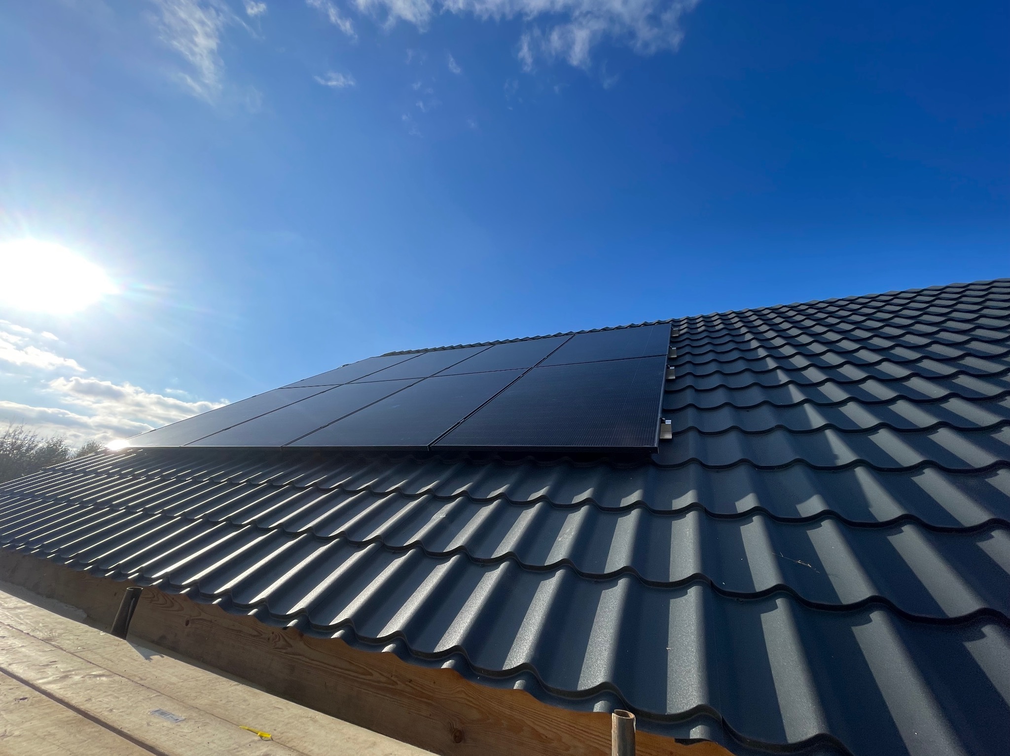 Panele słoneczne zamontowane na dachu z blachodachówki w słoneczny dzień, widoczne drewniane elementy konstrukcji dachu.