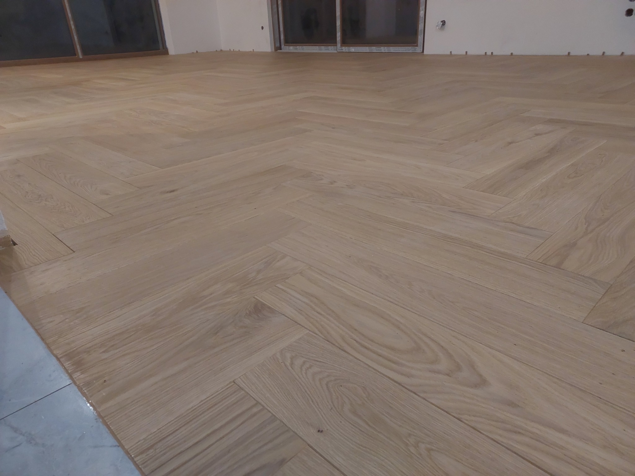 Ułożony parkiet w jodełkę w jasnym odcieniu drewna w Pruszkowie, widoczne listwy przypodłogowe i okno.