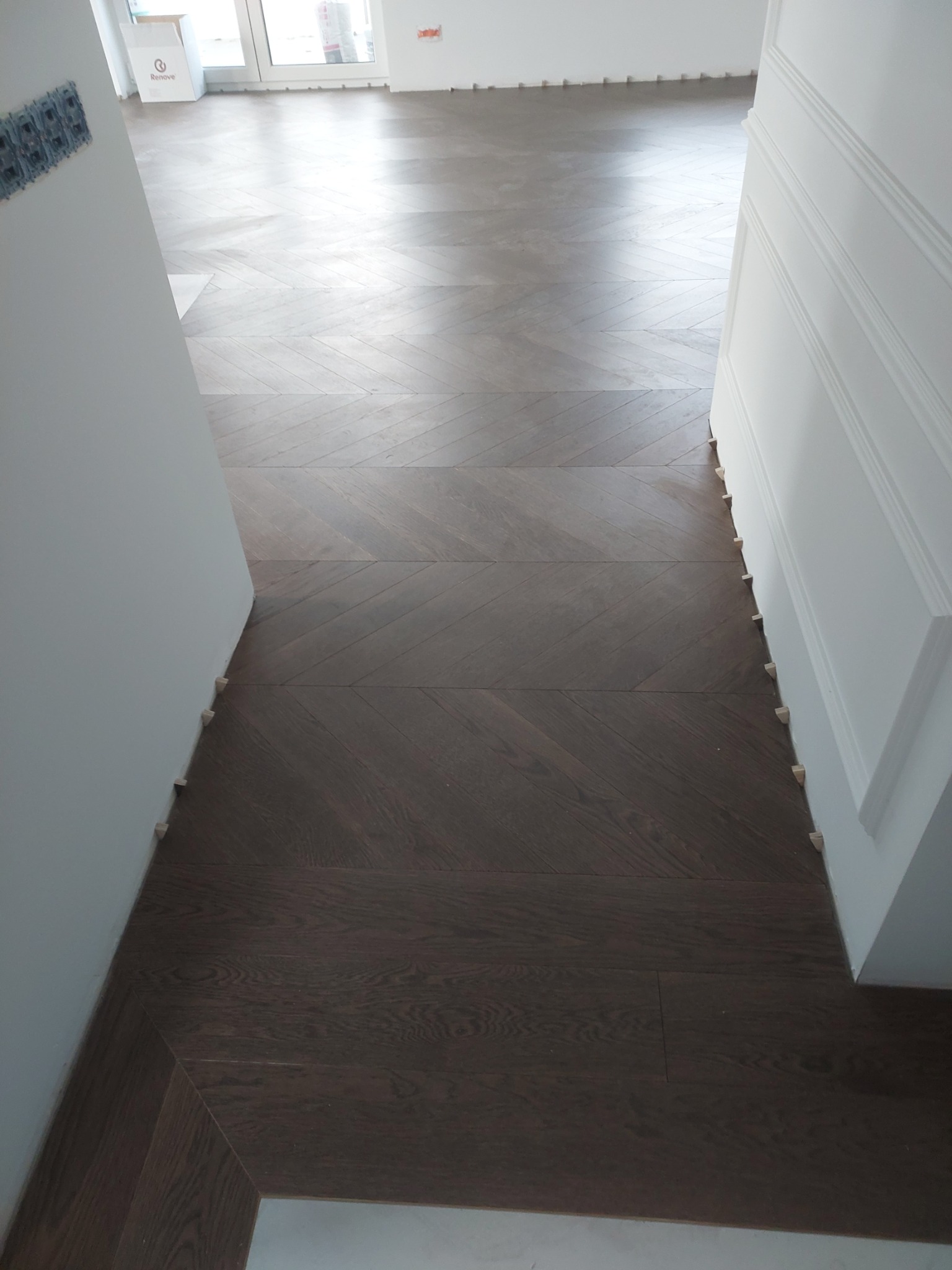 Ułożony parkiet w jodełkę, widoczne drewniane kliny dystansowe przy ścianach i listwach przypodłogowych.