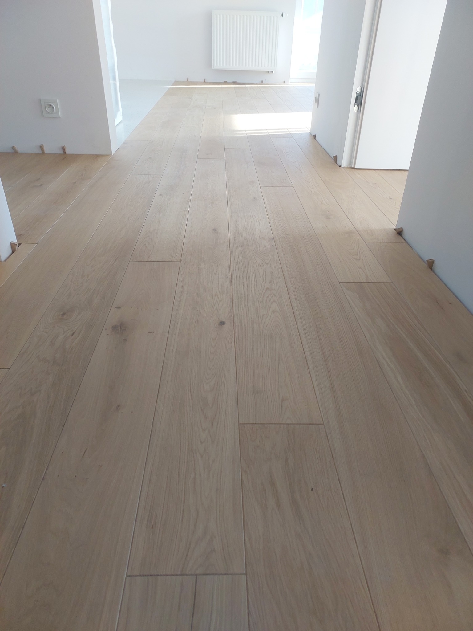 Jasna, drewniana podłoga z parkietu ułożona w nowym mieszkaniu, widoczne kliny dystansowe przy ścianach.