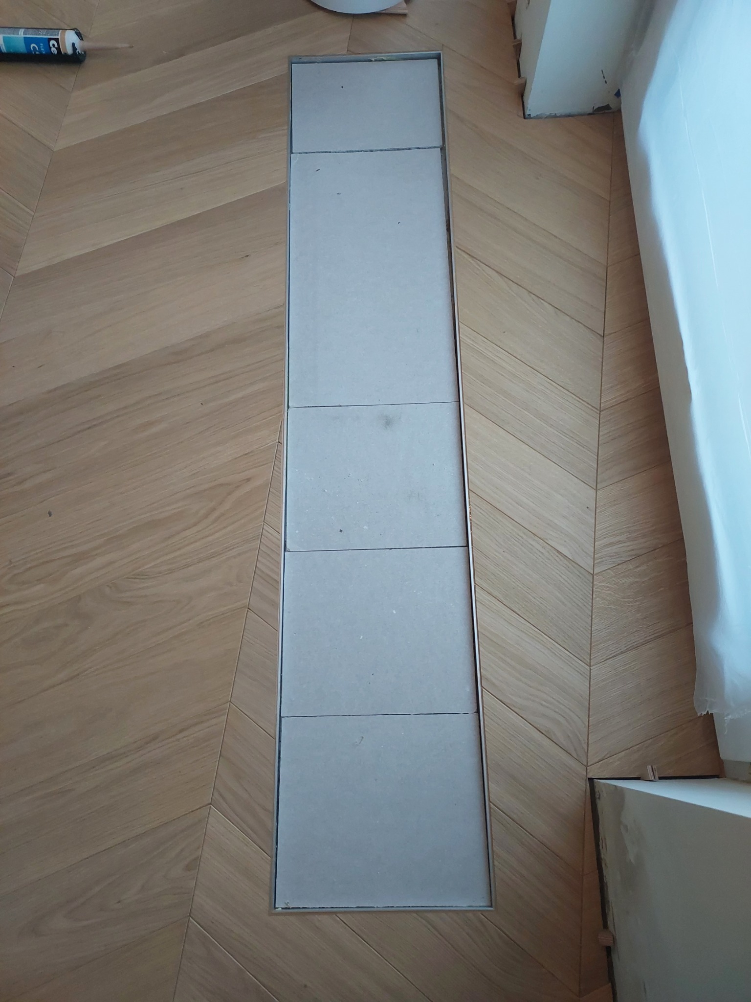 Ułożony parkiet w jodełkę z odkrytą przestrzenią na instalacje podłogowe, zabezpieczoną płytami.