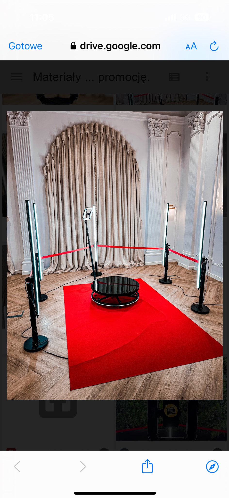 Okrągła platforma obrotowa otoczona czerwonym dywanem i lampami LED na tle eleganckiej ściany z kolumnami i drapowanymi zasłonami.