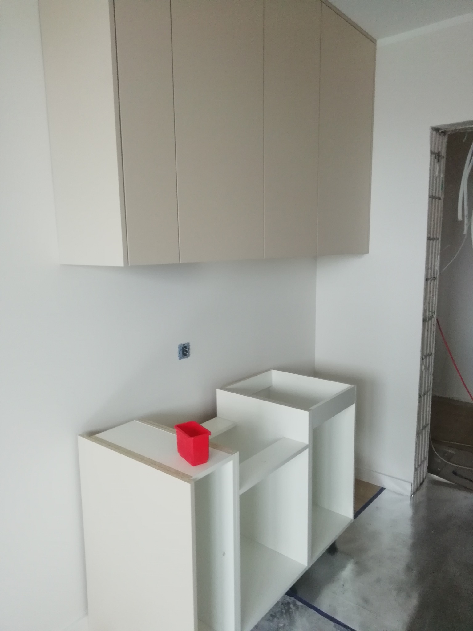 Montaż jasnych szafek kuchennych, widoczna czerwona miseczka na blacie i niezamaskowane gniazdko elektryczne na ścianie.