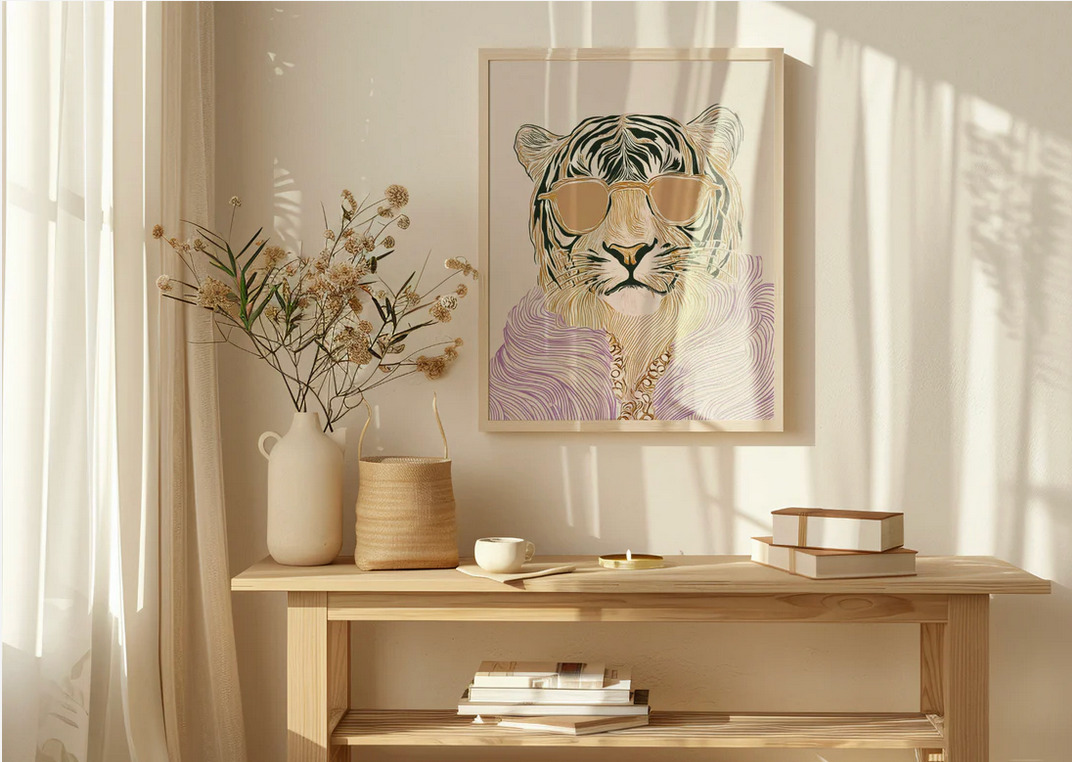 Oprawiony plakat z tygrysem w okularach i fioletowym futrze, stojący na drewnianej komodzie z wazonem kwiatów, koszykiem i stosem książek, oświetlony popołudniowym światłem.