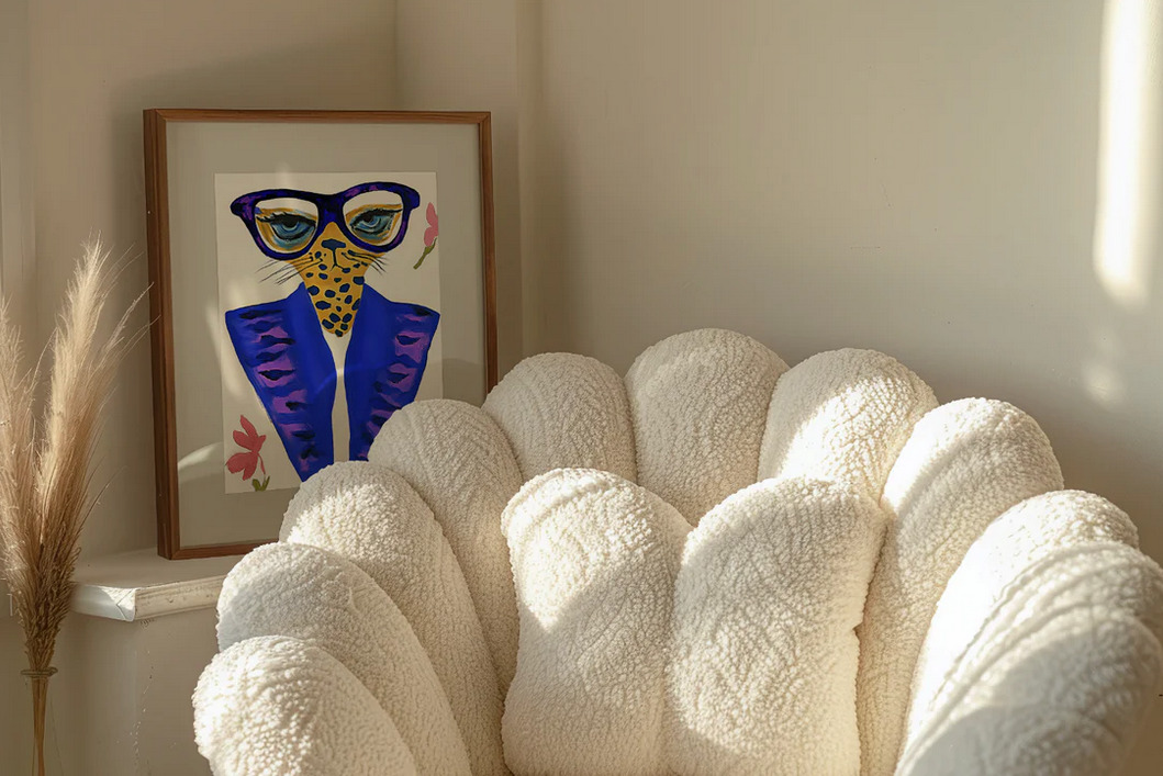 Oprawiony plakat z rysunkiem geparda w okularach i niebieskiej marynarce, obok puszysty, kremowy fotel muszelka i trawa pampasowa w rogu pokoju.